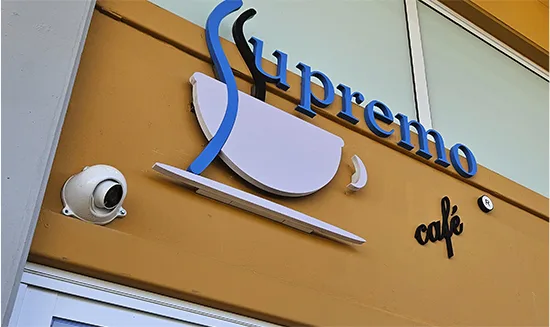 Detalhe do letreiro em PVC do Supremo Café na fachada, com câmera de segurança ao lado