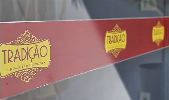 Faixa de segurança adesivada nas portas de vidro da Tradição, com o logotipo repetido