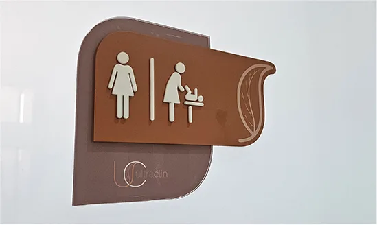 Placa de wayfinding da Ultraclin em acrílico, recortada no formato de folha, indicando banheiro e fraldário
